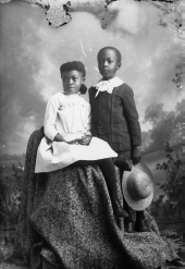 Seated girl and boy holding hat.